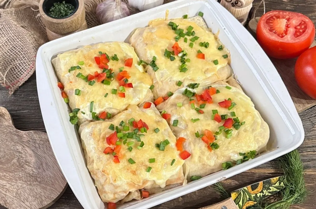 Cztery zapiekane naleśniki gyros jak z restauracji, posypane szczypiorkiem i papryką, w białym naczyniu żaroodpornym.