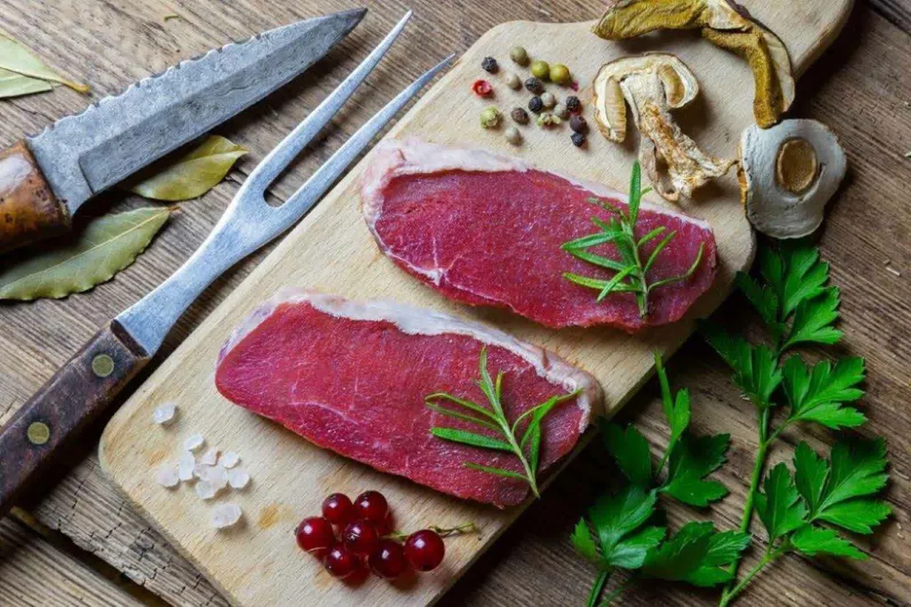 Dwa surowe steki wołowe, przyprawy, zioła i grzyby na desce. Czy myśliwi badają mięso przed przygotowaniem?