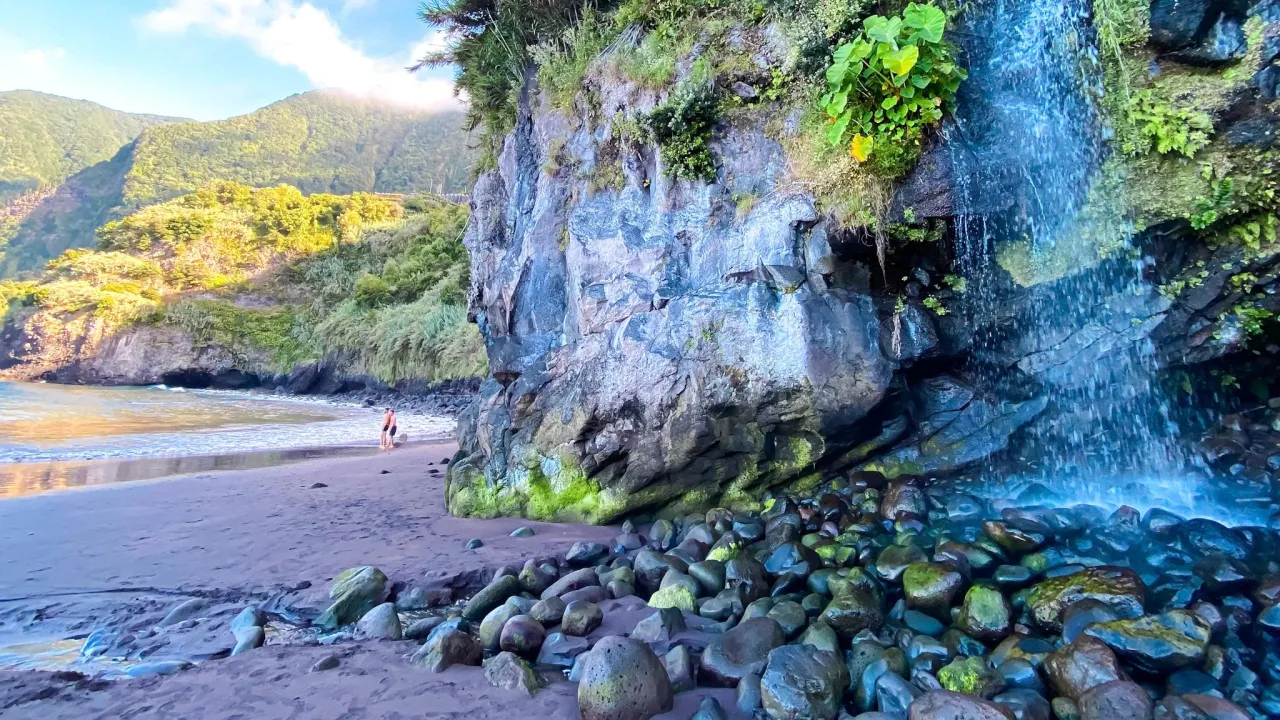 Wodospad spływa po skalnej ścianie na plażę z kamieniami. To jedno z madera najpiękniejsze miejsca.
