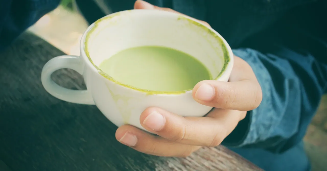 Dłonie trzymają biały kubek z zieloną matchą. Czy matcha pobudza? Ten nap&oacute;j może dodać energii.