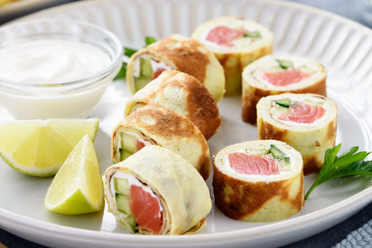 Sushi w naleśniku nazwa: rolki z łososiem, og&oacute;rkiem i serkiem, podane z dipem i limonką.