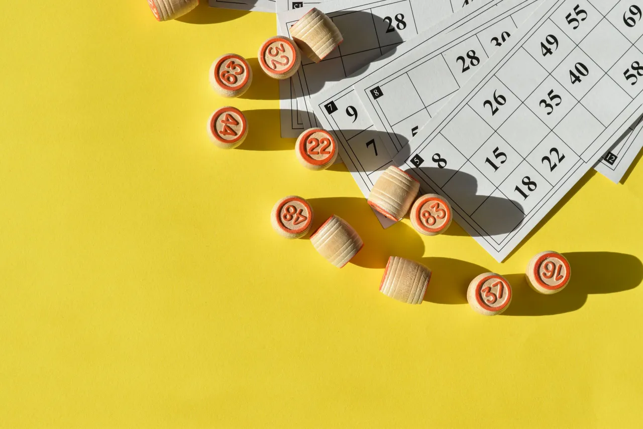 Drewniane krążki z numerami i karty do gry w bingo na żółtym tle.