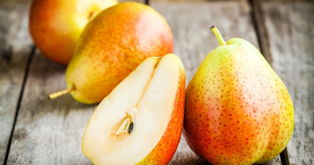 Gruszka, znana ze swoich właściwości leczniczych, prezentowana na drewnianym blacie. Poł&oacute;wka owocu ukazuje soczysty miąższ i pestki.