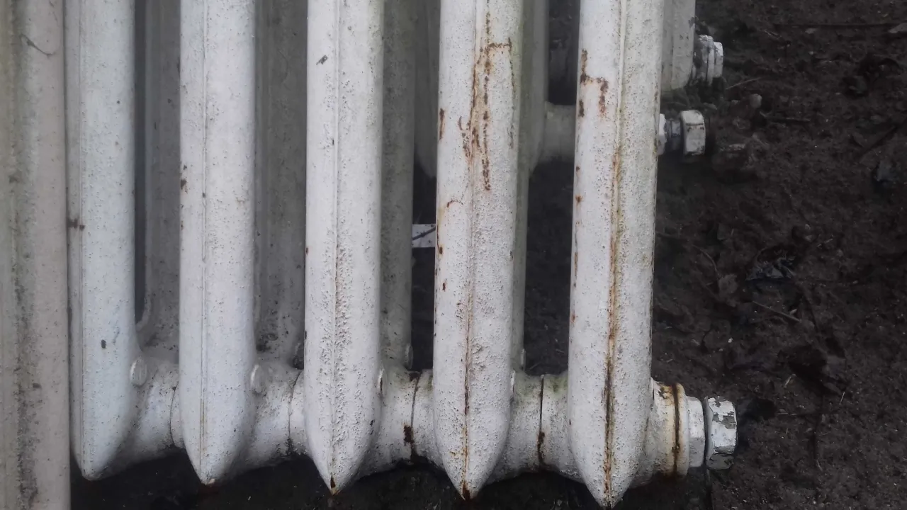 Stary, biały kaloryfer żeliwny, z widocznymi śladami rdzy. Zastanawiasz się, ile waży kaloryfer żeliwny? Jest ciężki!