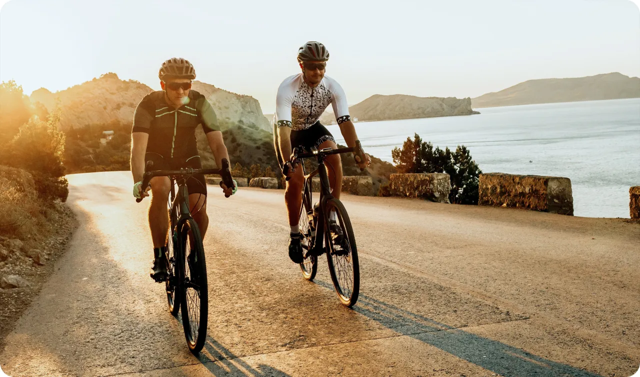 Dw&oacute;ch kolarzy jedzie po malowniczej drodze nad morzem. Czy to trening na czczo, czy po jedzeniu? Słońce zachodzi, tworząc piękne cienie.