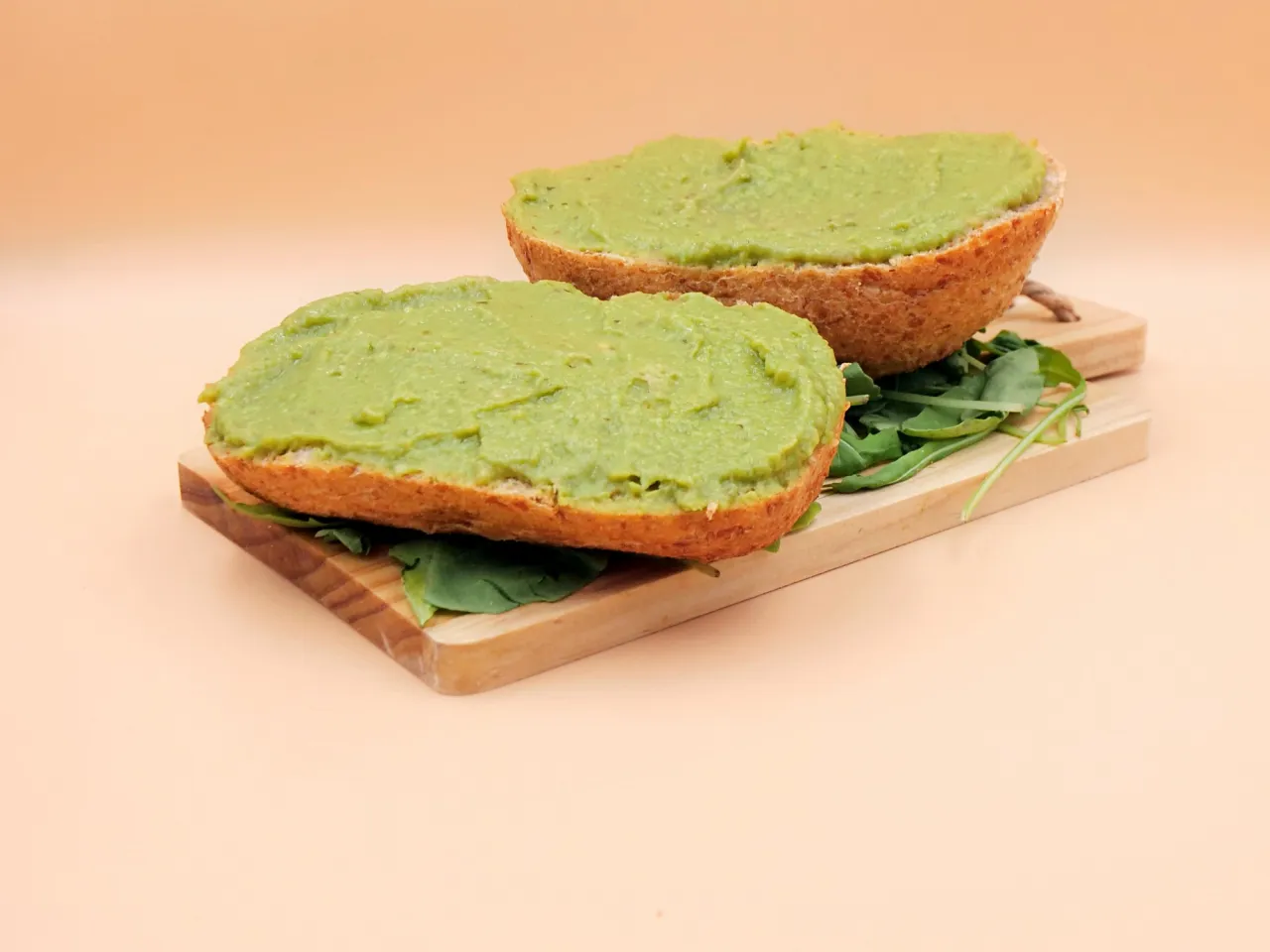 Dwie połówki bułki z zielonym guacamole, ułożone na desce z rukolą. Idealne do jedzenia na śniadanie.
