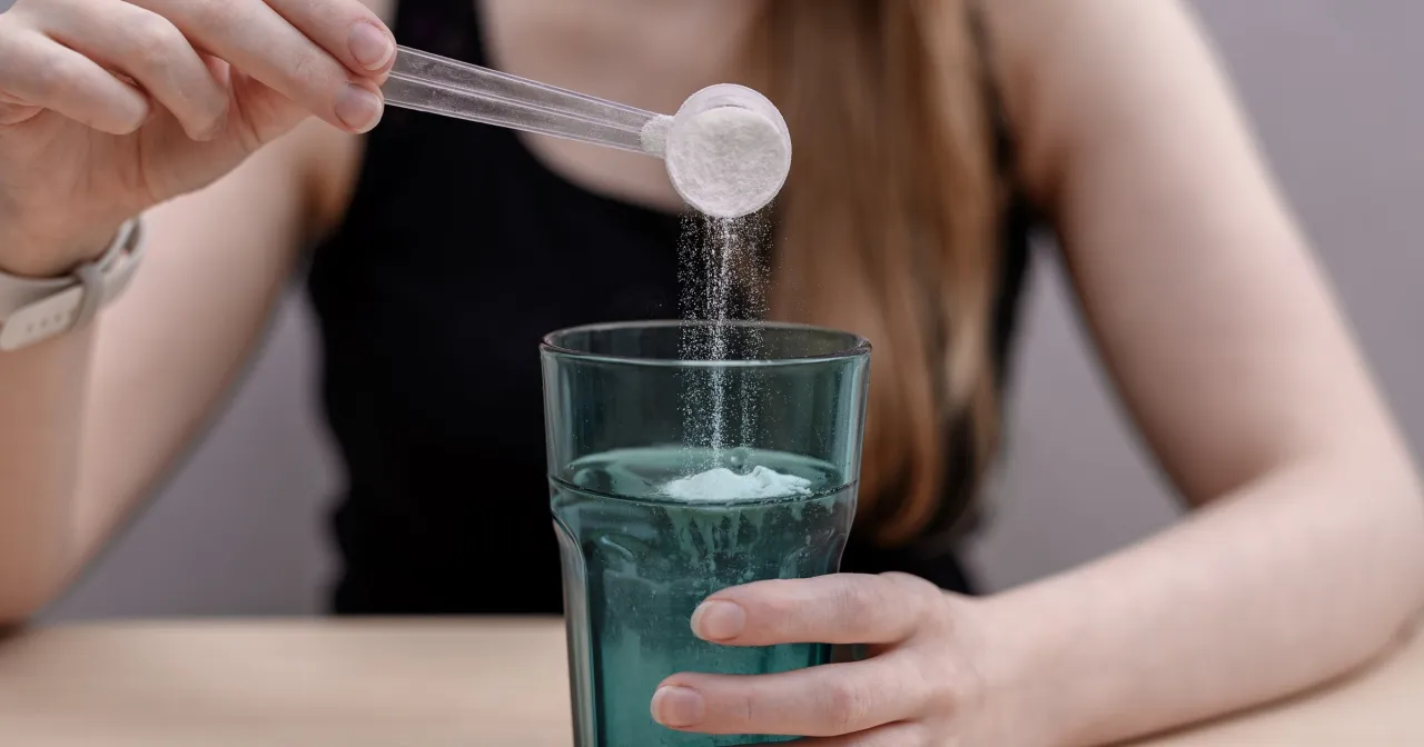 Kiedy pić kolagen? Kobieta wsypuje proszek do szklanki z wodą, przygotowując zdrowy nap&oacute;j.