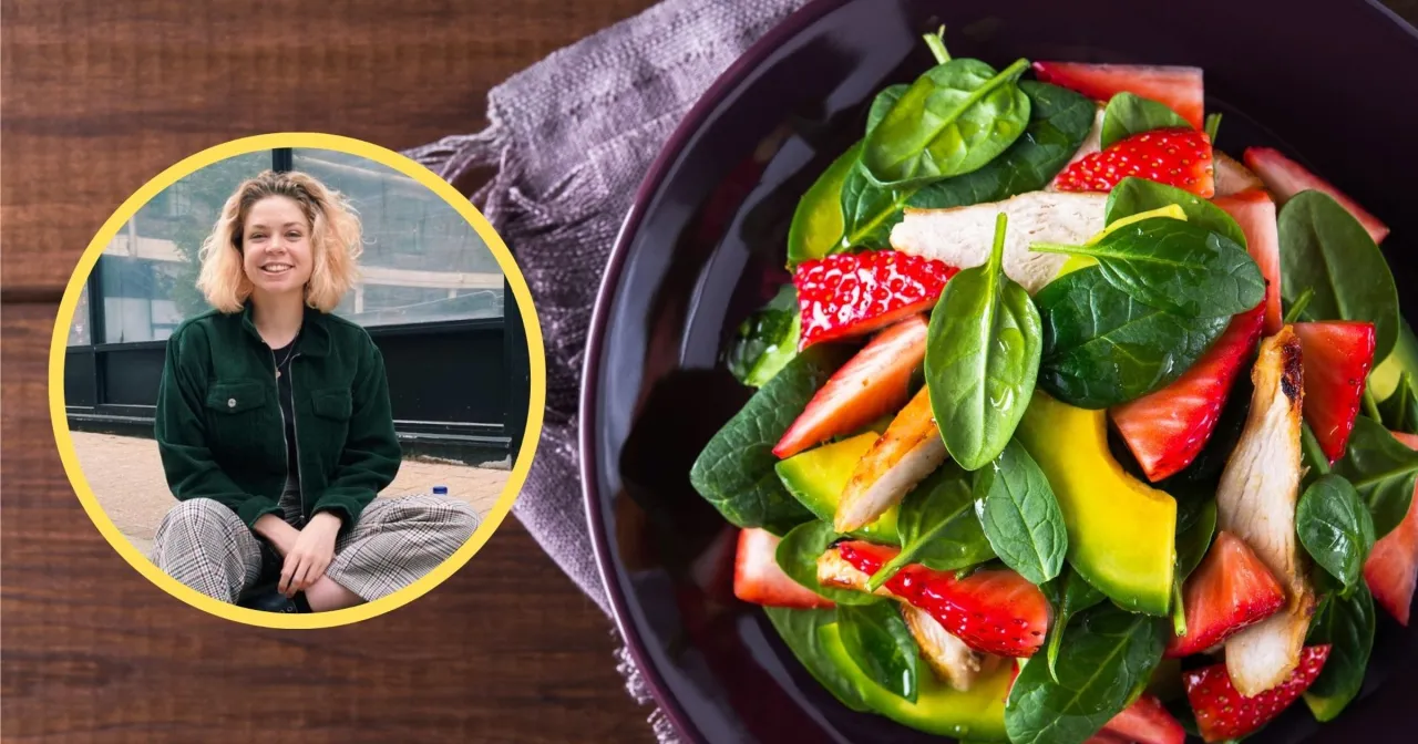 Uśmiechnięta dziewczyna i talerz pełen świeżych składników: szpinak, truskawki, awokado i kurczak. Idealna zdrowa kolacja.