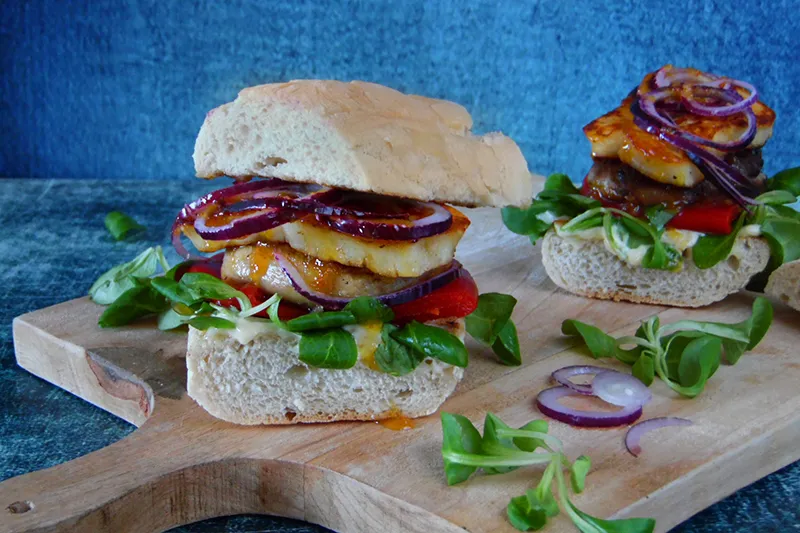 r&oacute;żne składniki na burgera, deska do krojenia, świeże warzywa, mięso, ser, bułka