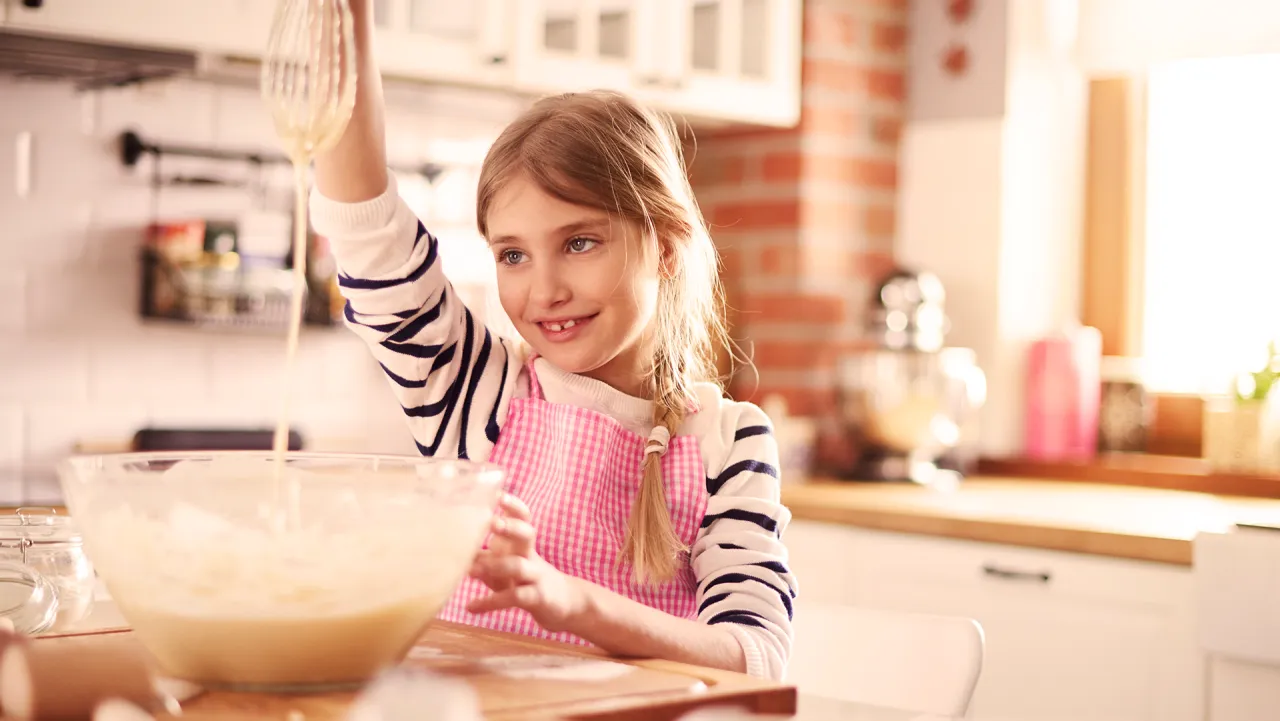 Uśmiechnięta dziewczynka w fartuszku miesza ciasto. Idealny przepis na to, co może ugotować 10 latka.