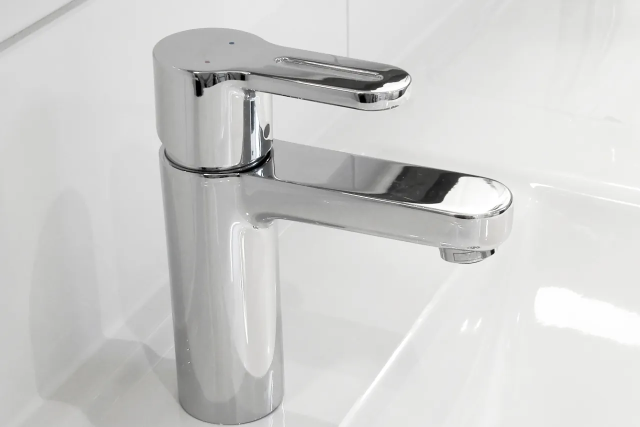 Błyszczący, chromowany kran jednouchwytowy nad białą umywalką. Poradnik: jak rozebrać kran.