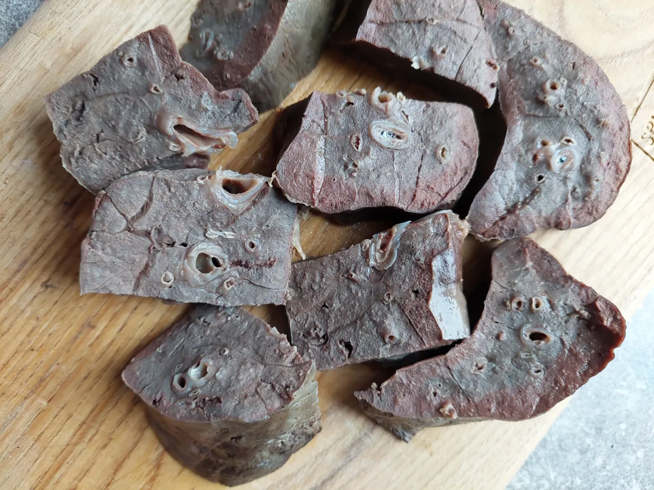 Kawałki wieprzowych płuc na desce. Czy płuca wieprzowe są zdrowe? Widać liczne, okrągłe otwory i nieregularną strukturę tkanki.