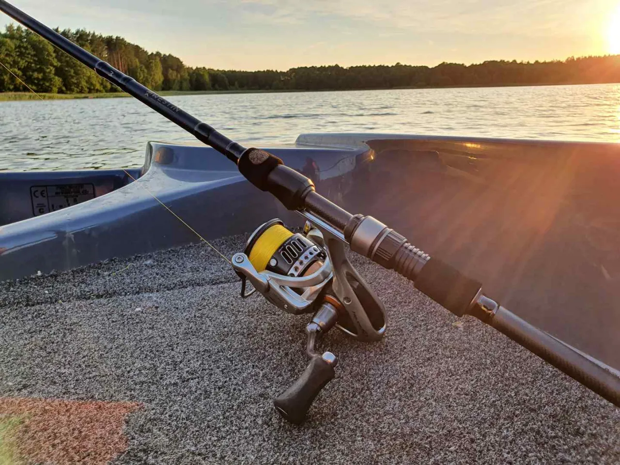 Wędka na sandacza gotowa do akcji. Złoty zach&oacute;d słońca nad jeziorem i sprzęt wędkarski w łodzi.