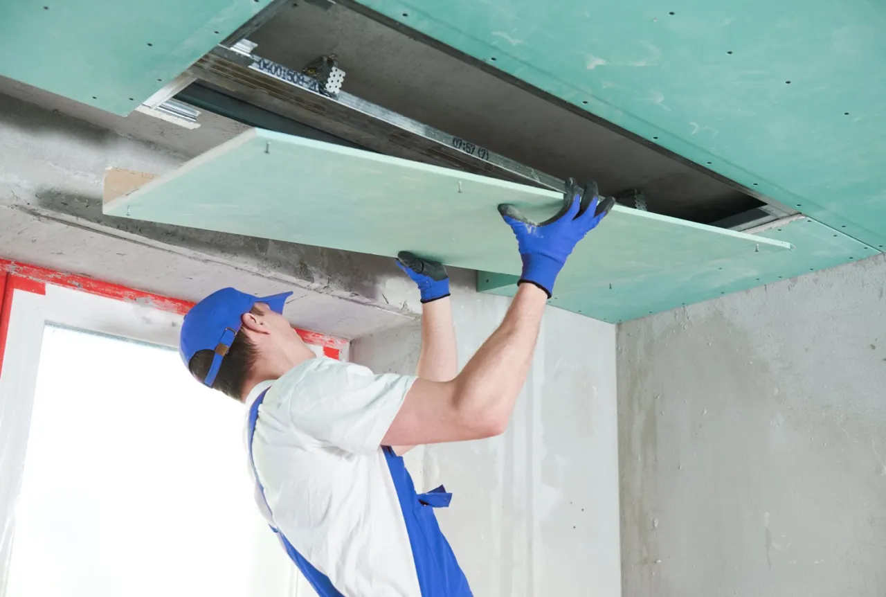 Budowlaniec montuje płytę karton gips na suficie. Zastanawiasz się, ile waży płyta karton gips? To zależy od jej grubości i rodzaju.