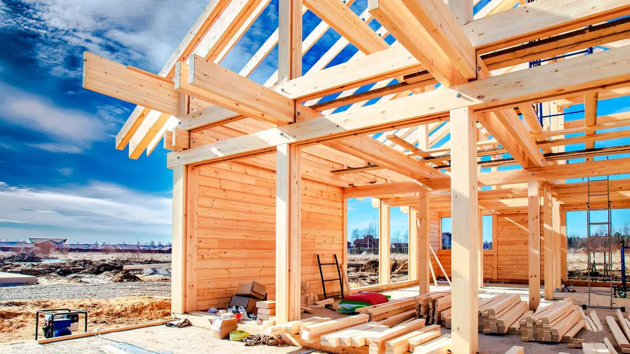 Drewniana konstrukcja domu szkieletowego w budowie. Widać belki stropowe i dachowe. Materiały budowlane leżą na ziemi.