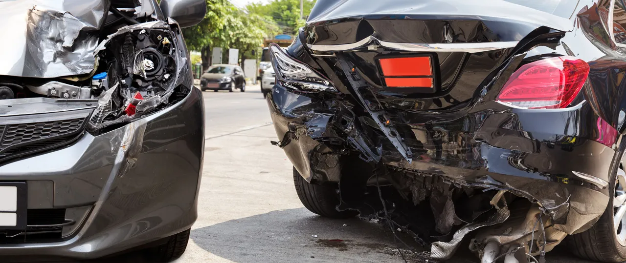 Dwa mocno uszkodzone samochody po wypadku. Zniszczone przody i tyły pojazd&oacute;w świadczą o konieczności likwidacji szk&oacute;d komunikacyjnych.