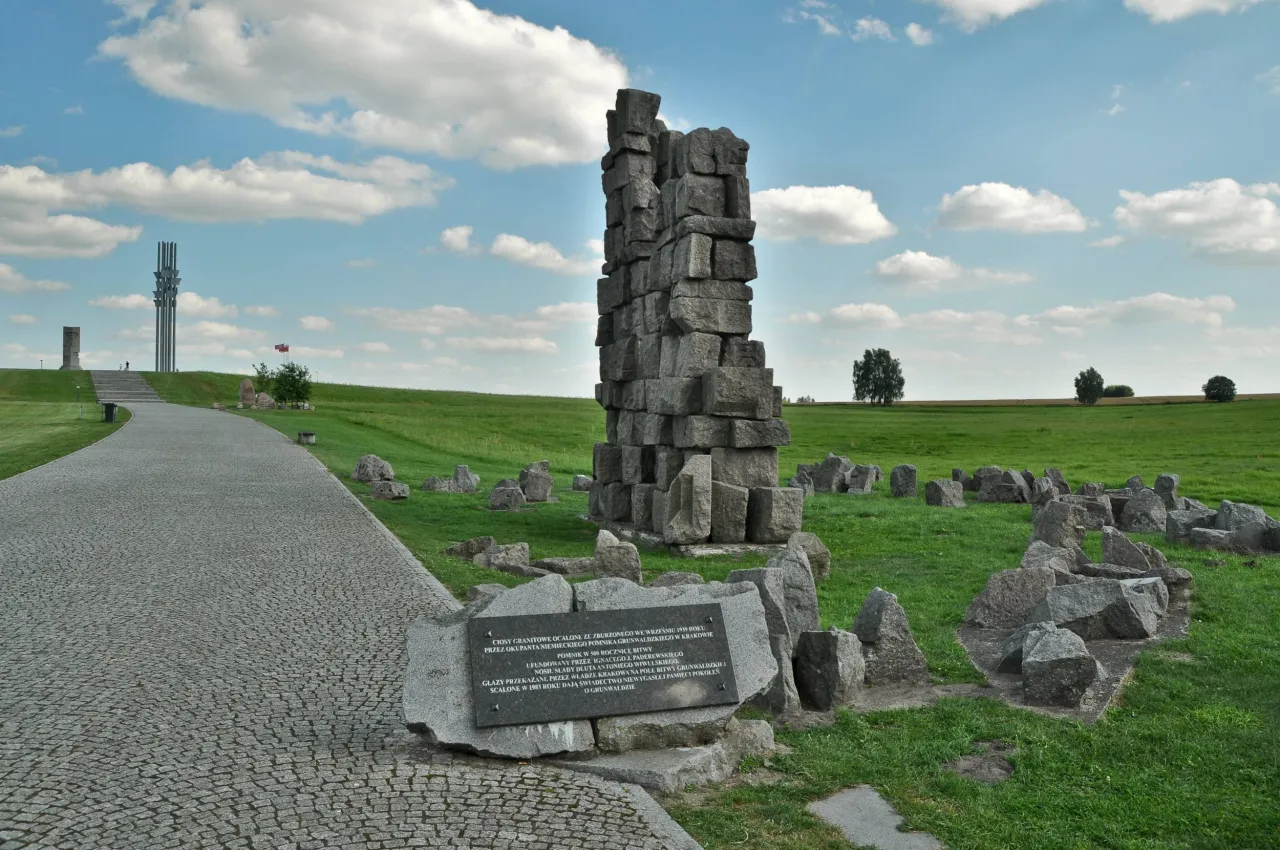 Pomnik Grunwaldzki, symbolizujący miejsce bitwy, gdzie leży Grunwald na mapie Polski. Kamienne ruiny i tablica pamiątkowa na tle nieba.