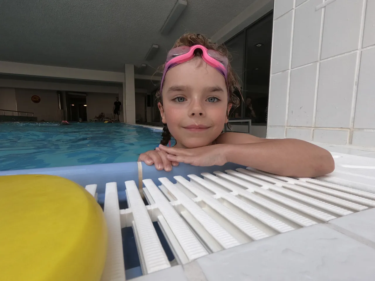Uśmiechnięta dziewczynka w goglach na basenie. Zastanawia się, ile trwa nauka pływania, ale już świetnie się bawi!