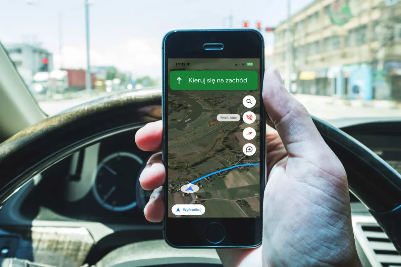 Telefon w dłoni kierowcy pokazuje nawigację. Używanie telefonu podczas jazdy grozi mandatem i punktami karnymi.