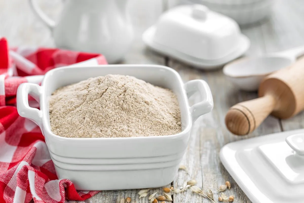 Mąka krupczatka w białej misce, obok wałek i czerwono-biała ściereczka. Czy krupczatka to mąka ziemniaczana? Nie, to mąka pszenna gruboziarnista.