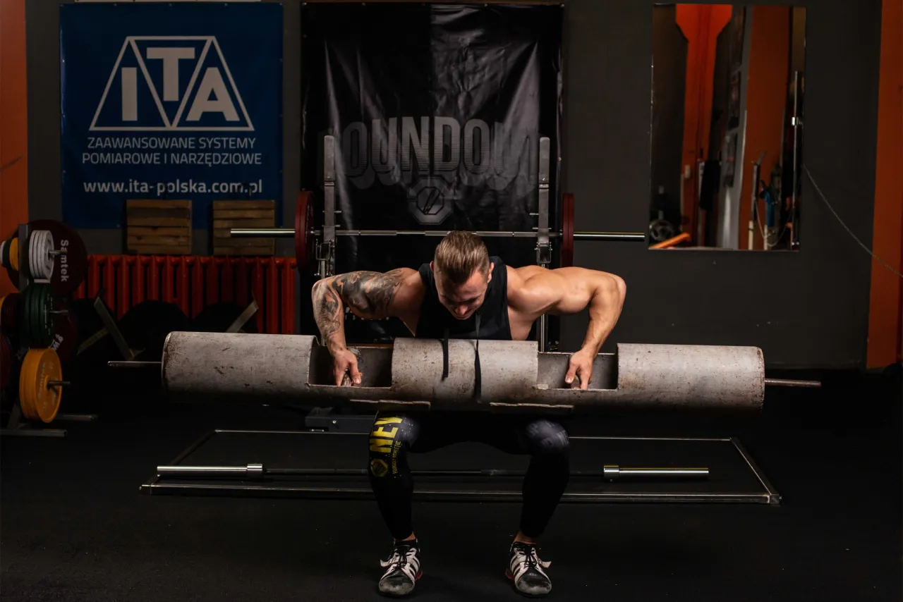 osoba trenująca na siłowni z planem treningowym