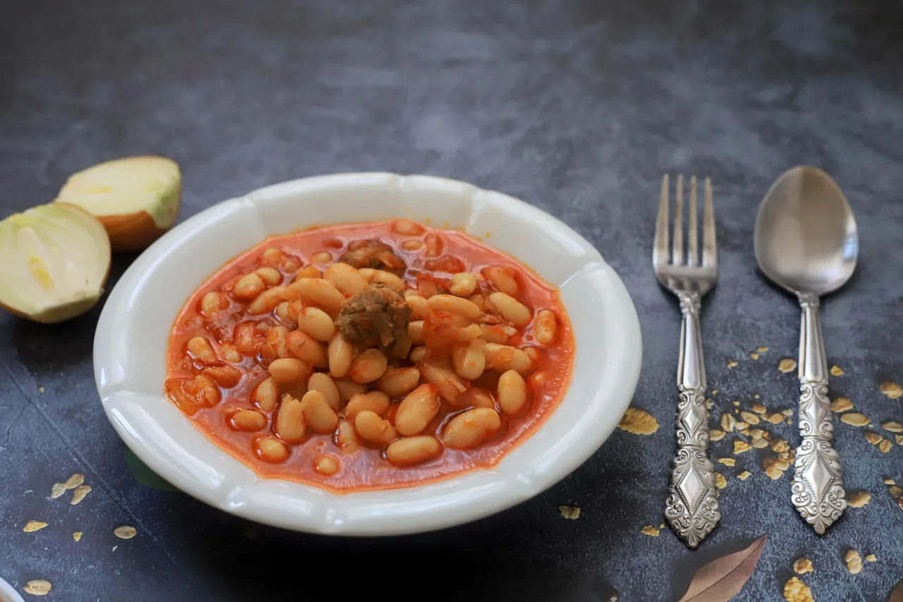 Fasola po bretońsku z klopsikiem, cebulą i sztućcami. Zastanawiasz się, jakie przyprawy do fasoli po bretońsku?