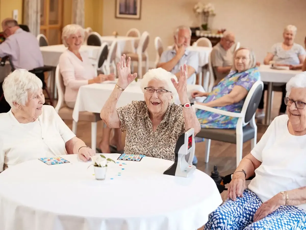 Seniorzy grają w bingo, śmiejąc się i bawiąc. To miejsce, gdzie troska i radość idą w parze, a cena za dom seniora jest adekwatna do jakości życia.