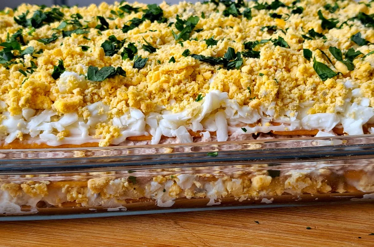 Warstwowa sałatka z tuńczyka, jajek i majonezu, posypana posiekaną natką pietruszki. Idealna, gdy zastanawiasz się, jak zrobić sałatkę z tuńczyka.