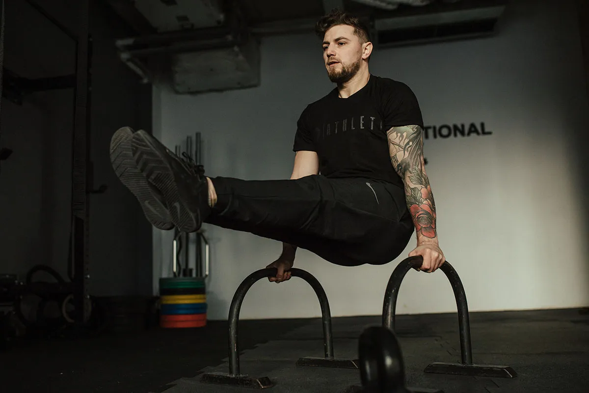 Mężczyzna z tatuażami wykonuje ćwiczenie na poręczach. Intensywny trening, jak w metodzie tabata, wymaga siły i wytrzymałości.