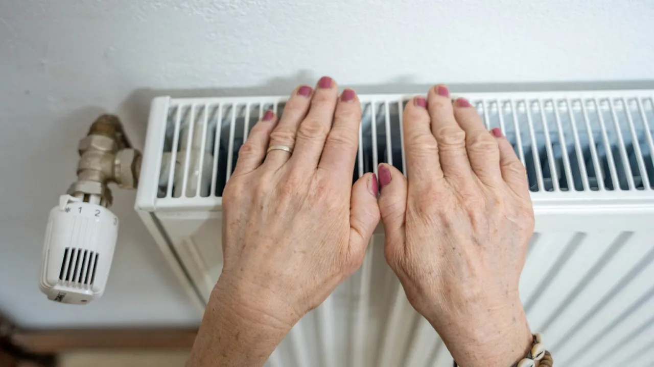 Dłonie ogrzewają się przy grzejniku, szukając optymalnej temperatury w domu. Termostat ustawiony na 2.