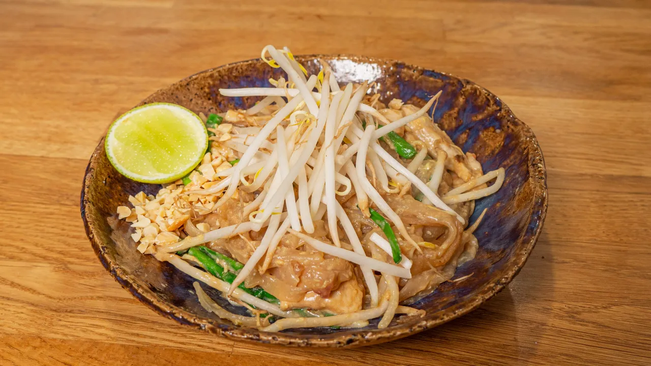 Pyszne pad thai z jajkiem, kiełkami, orzeszkami i limonką na rustykalnym talerzu.