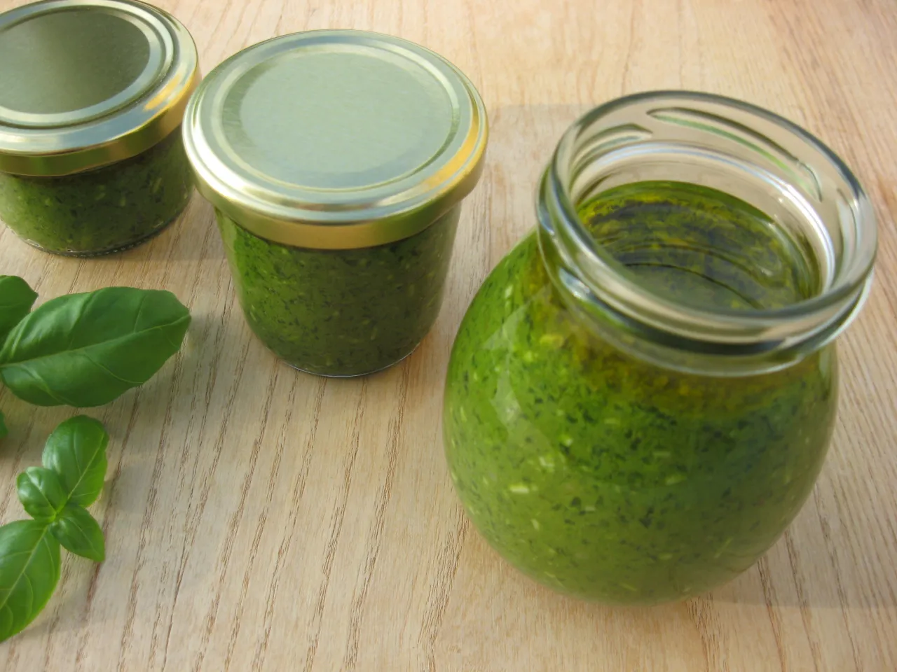 Słoiki z domowym pesto z bazylii, gotowe na zimę. Świeże liście bazylii obok.