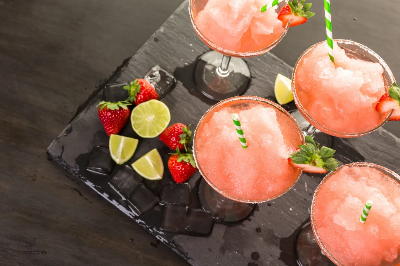 Margarita klasyczna kontra Margarita truskawkowa. Mrożone drinki z truskawkami i limonkami na kamiennej desce.