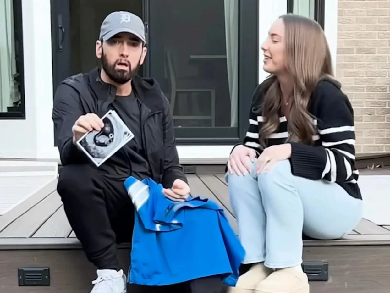Eminem trzyma zdjęcie USG, sugerując, ile dzieci ma Eminem. Obok siedzi kobieta.