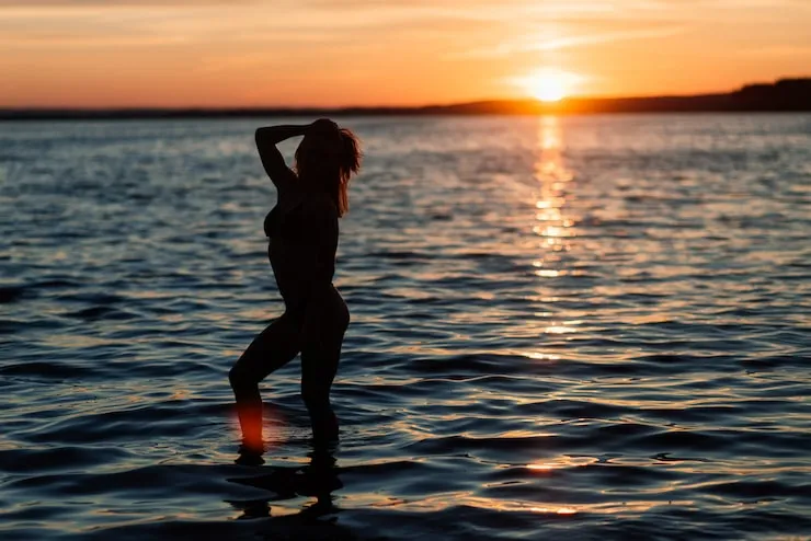 Kobieta pozuje na plaży o zachodzie słońca