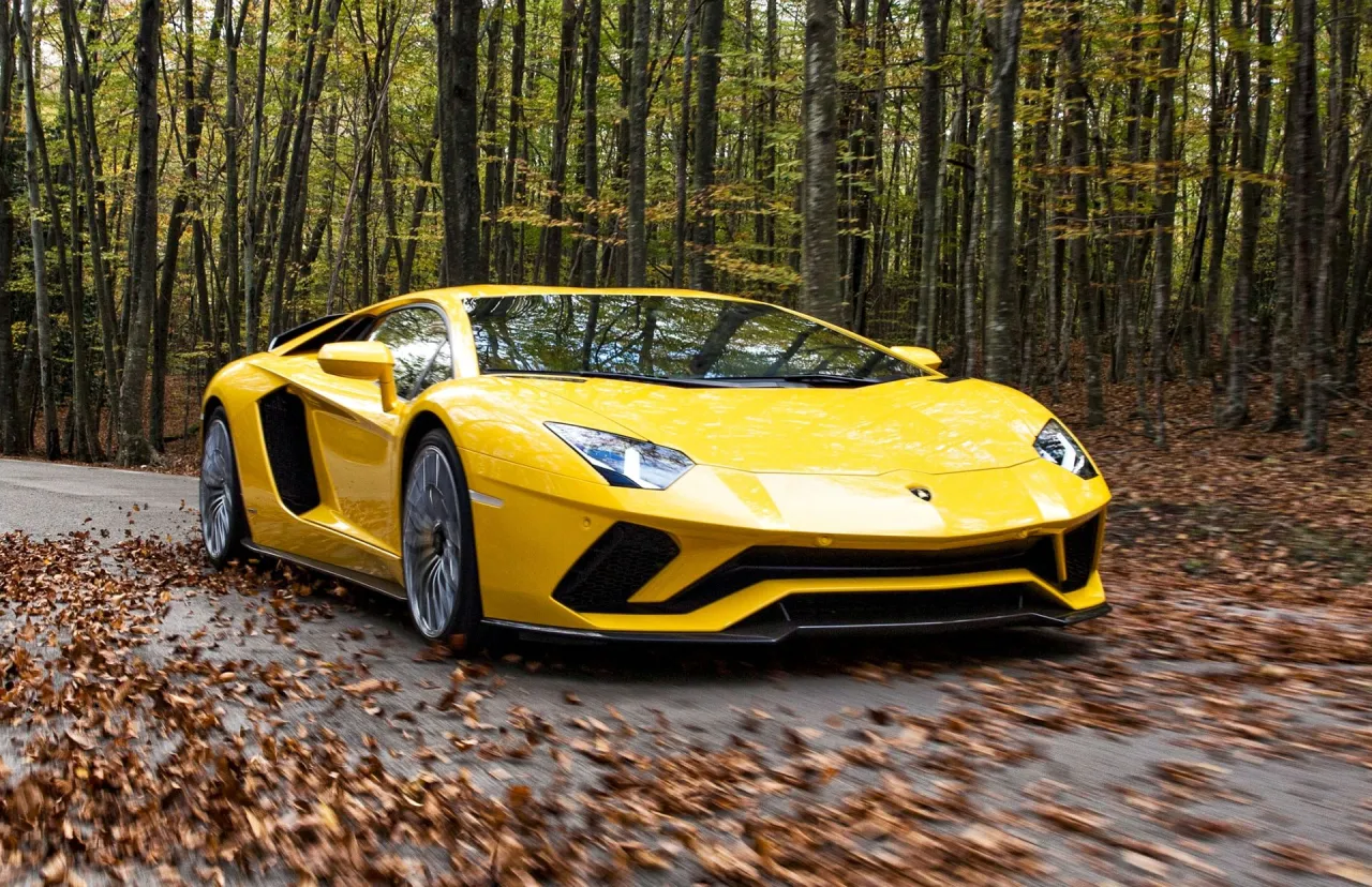 Ż&oacute;łte Lamborghini Aventador mknie przez jesienny las. Zastanawiasz się, ile kosztuje najtańsze Lamborghini?