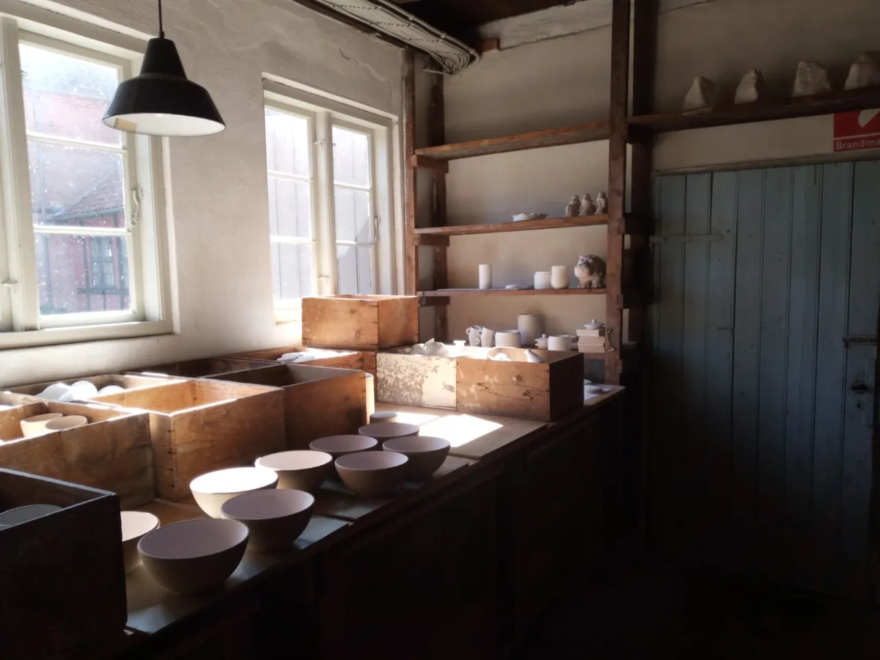 wnętrze przytulnej pracowni ceramicznej z p&oacute;łkami pełnymi gotowych prac