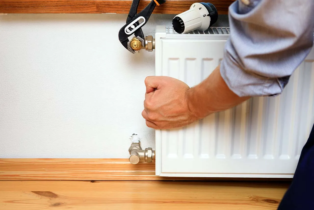 Ręka z kluczem nastawnym przy zaworze grzejnika, pokazująca, jak zakręcić grzejnik bez pokrętła.