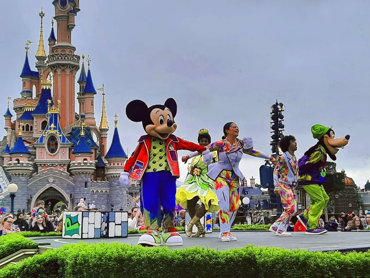 Myszka Miki i przyjaciele na scenie przed zamkiem w Disneylandzie Paryż. Kolorowe stroje i radosna atmosfera, typowe dla atrakcji tego miejsca.
