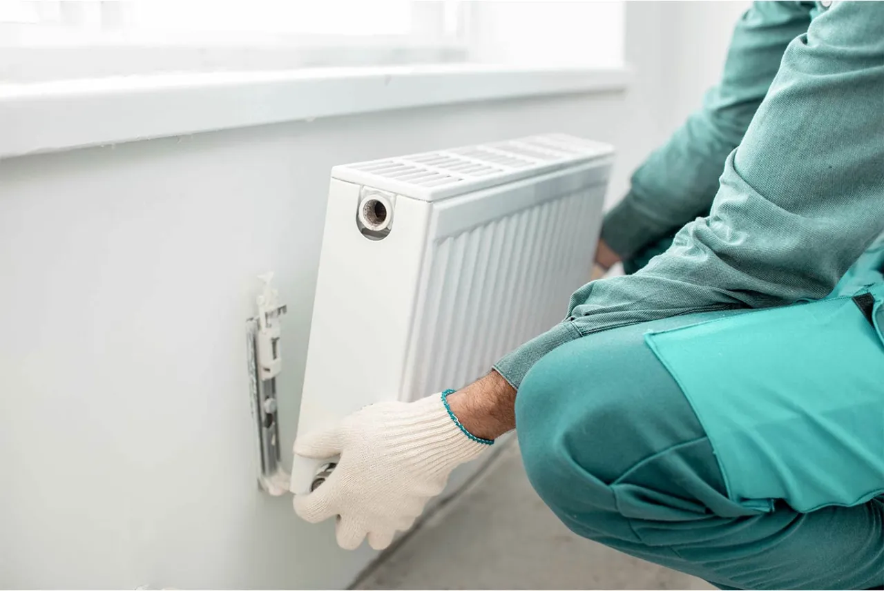 Instalator w białej rękawiczce montuje nowy kaloryfer. Dowiedz się, jak wymienić kaloryfer w bloku.