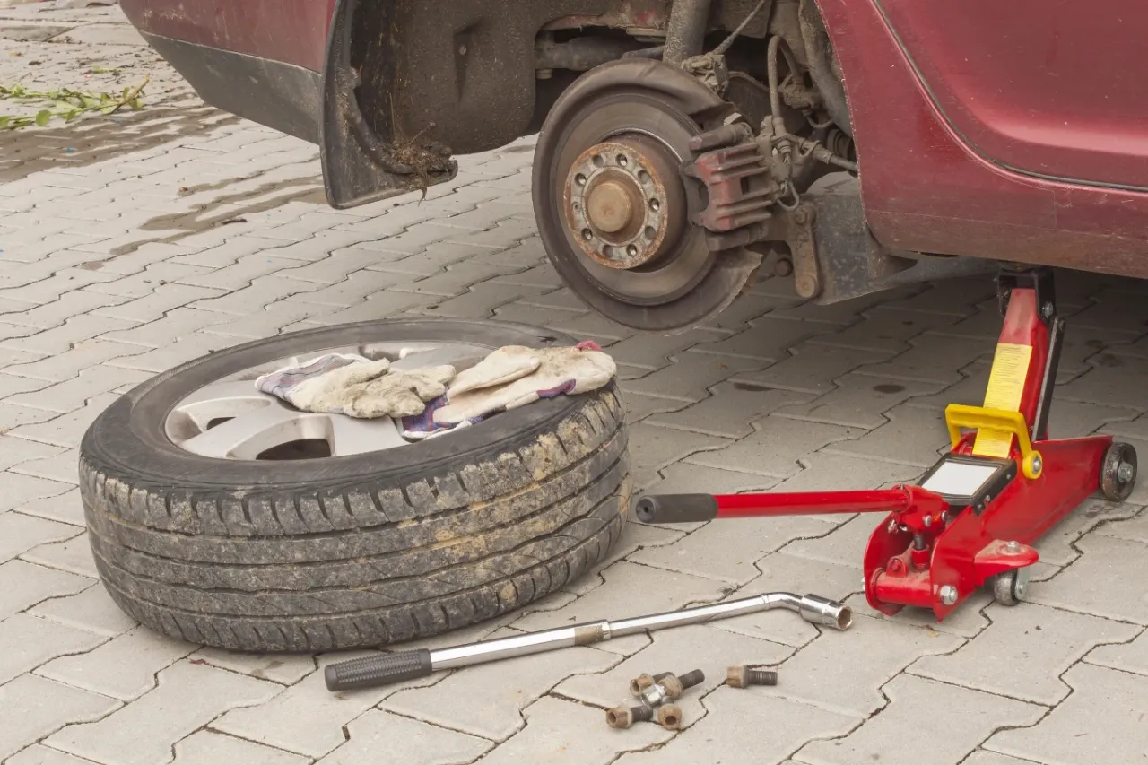 Wymiana koła. Czy koło zapasowe jest obowiązkowe? Podnośnik, klucz i śruby leżą obok.