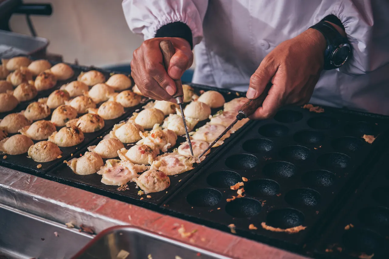 Ręce obracają kulki takoyaki na specjalnej patelni. To idealny takoyaki przepis, kt&oacute;ry pozwala stworzyć te japońskie przysmaki.
