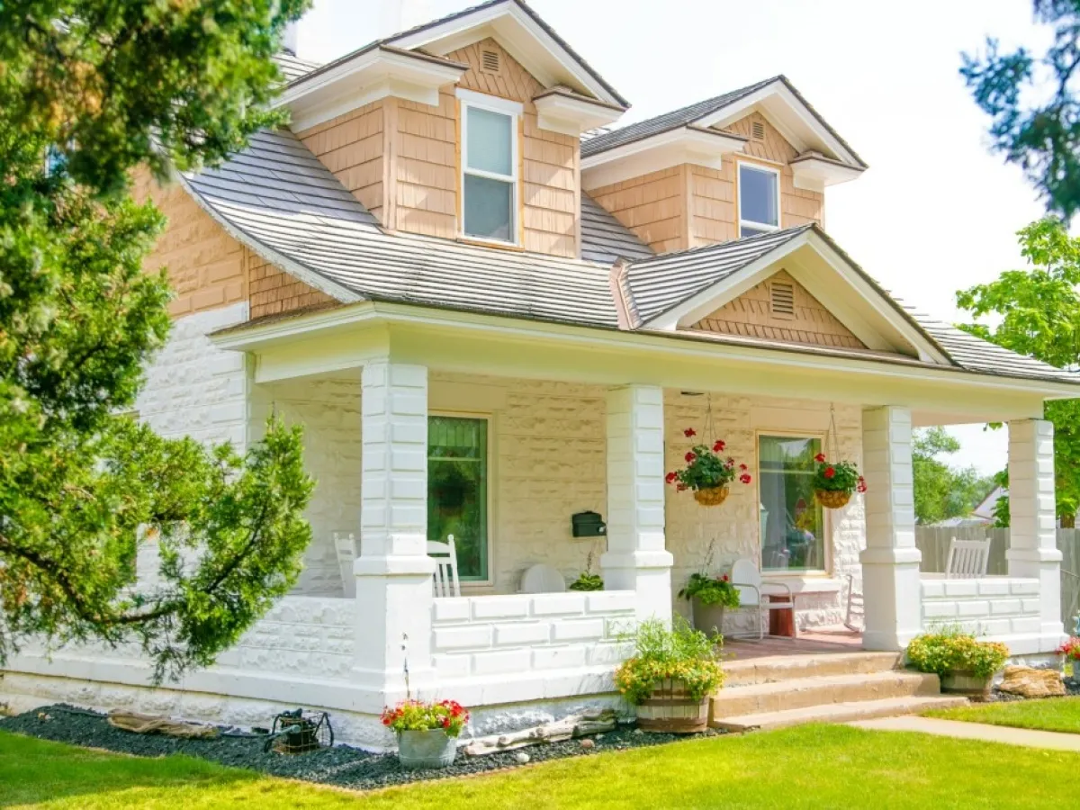 Piękna biała elewacja domu z kamienia i drewna, z werandą i wiszącymi donicami z kwiatami.