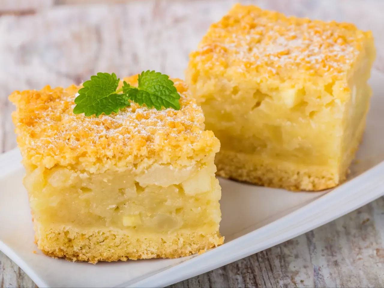 Dwa kawałki szarlotki z kruszonką i miętą. Idealny przykład, jak się robi szarlotkę, która zachwyca smakiem i wyglądem.