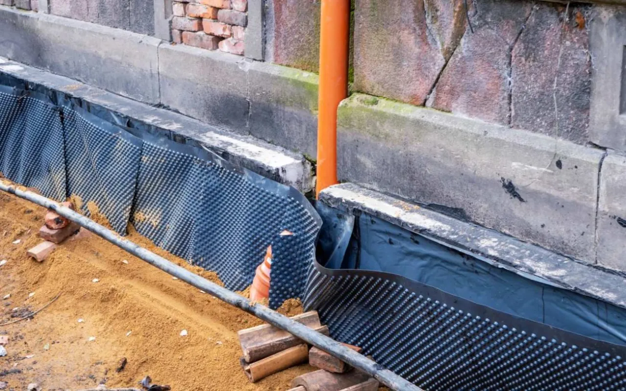 Prace przy starym domu: folia kubełkowa i rura pomarańczowa wskazują na metody, jak ocieplić fundament starego domu.