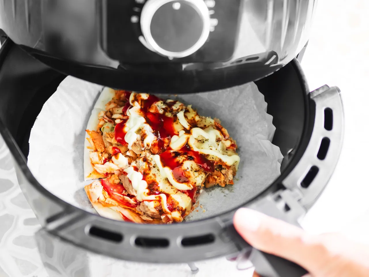 Jak odgrzać pizzę w frytkownicy beztłuszczowej? Kawałek pizzy z kurczakiem i sosami w koszu frytkownicy.