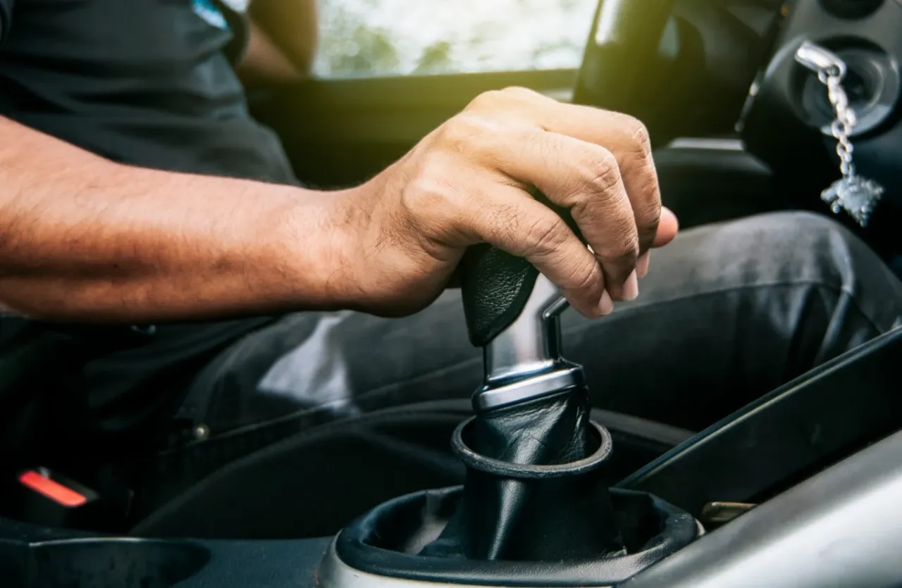 Dłoń kierowcy na dźwigni zmiany bieg&oacute;w, pokazująca, jak hamować silnikiem, redukując biegi.