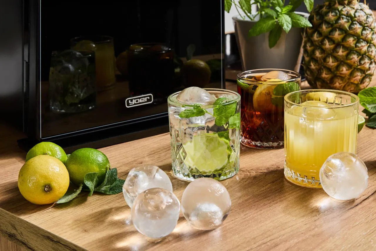 Orzeźwiające drinki z kruszonym lodem i owocami. Obok leżą cytryny, limonki i ananas.