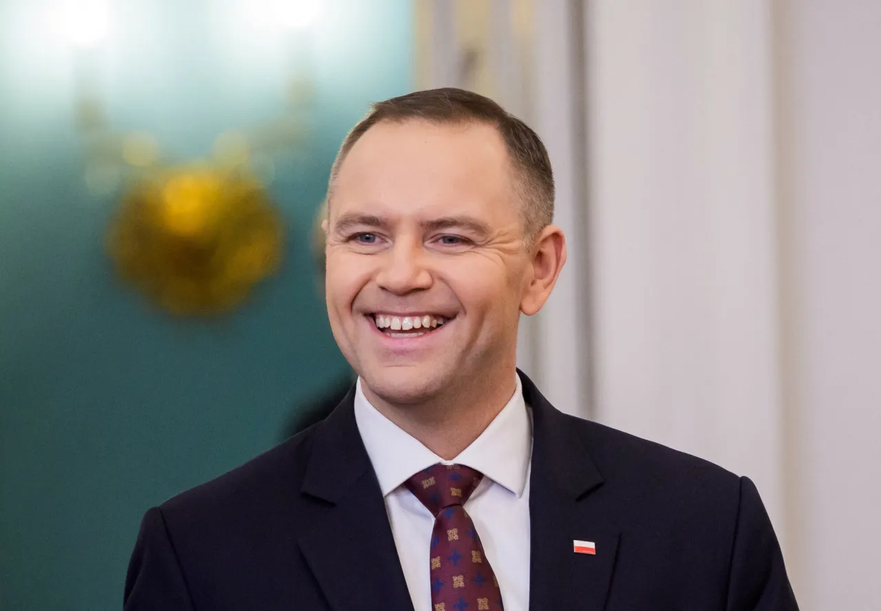 Uśmiechnięty mężczyzna w garniturze, z przypinką z polską flagą. W tle widać złoty element i zieloną ścianę. Ile lat ma Duda?