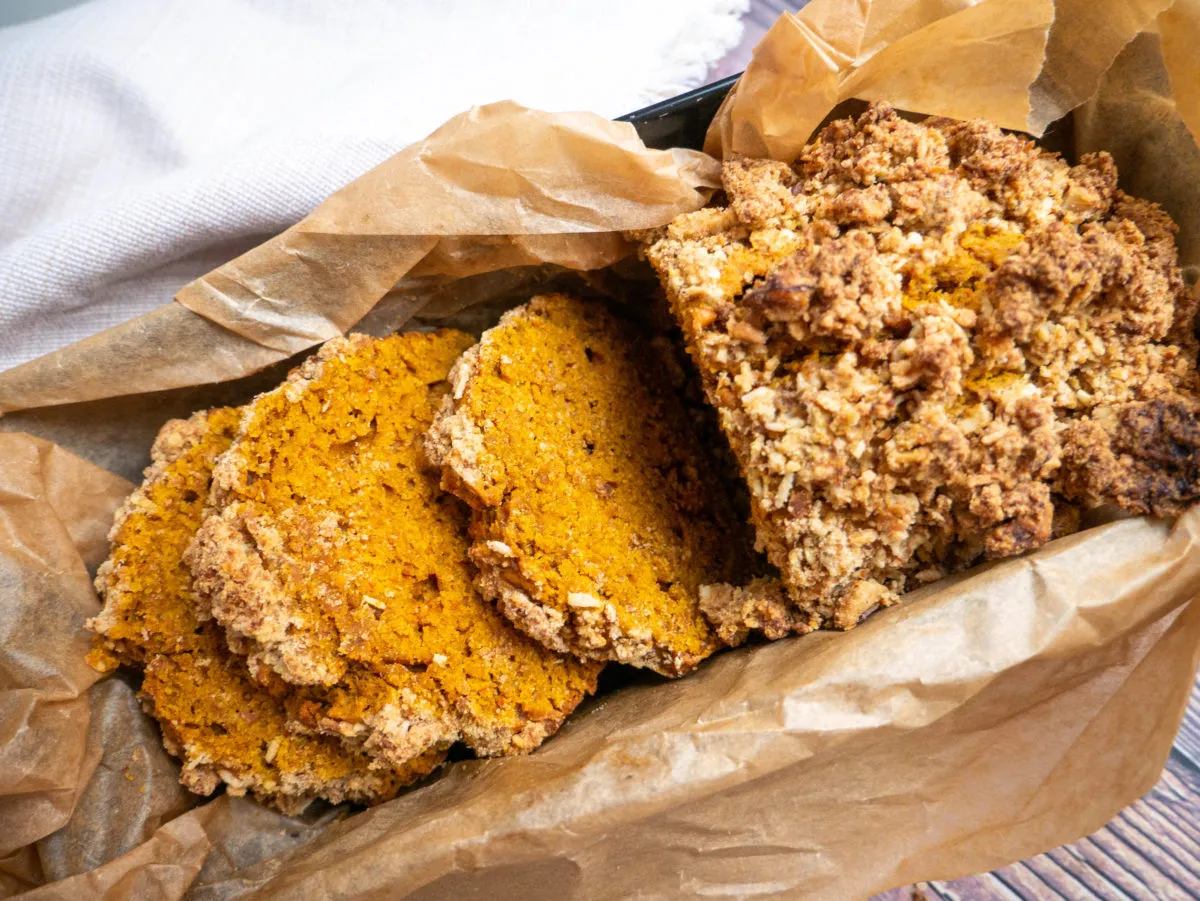 Okrasa łamie przepisy ciasto dyniowe. Kromki pachnącego, pomarańczowego ciasta dyniowego z chrupiącą kruszonką, wyłożone papierem do pieczenia.